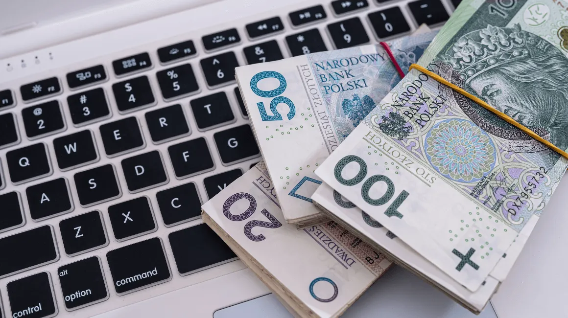 Plik polskich banknotów leży na klawiaturze laptopa
